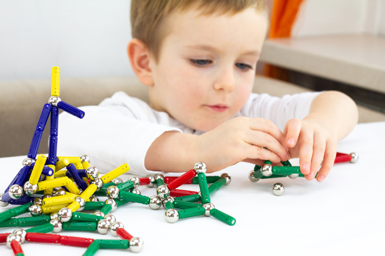 Cute child playing with lots of colorful magnet on white background